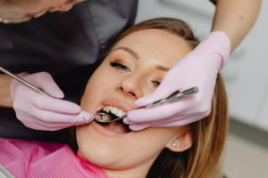 A dentist wearing light pink gloves inspecting a patient’s teeth