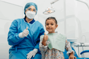 dentist sitting next to a young girl, both giving a thumbs-up gesture and smiling Image