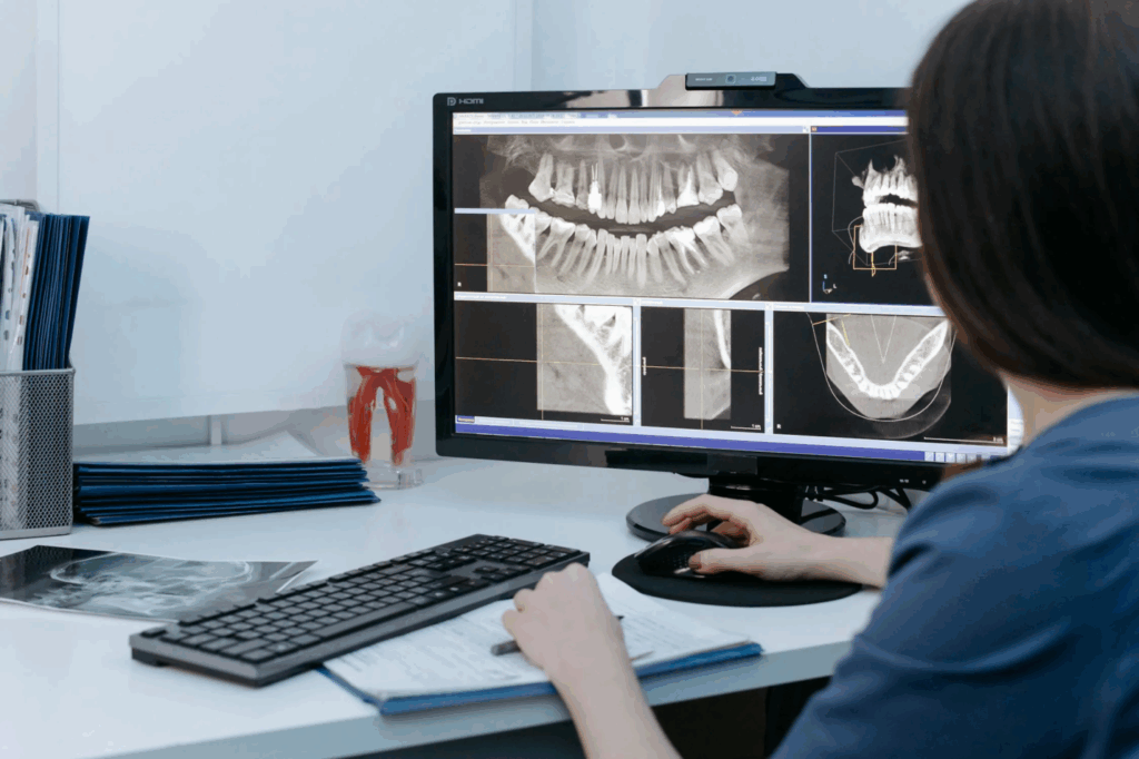 A dentist reviewing panoramic dental X-rays displayed on a computer monitor