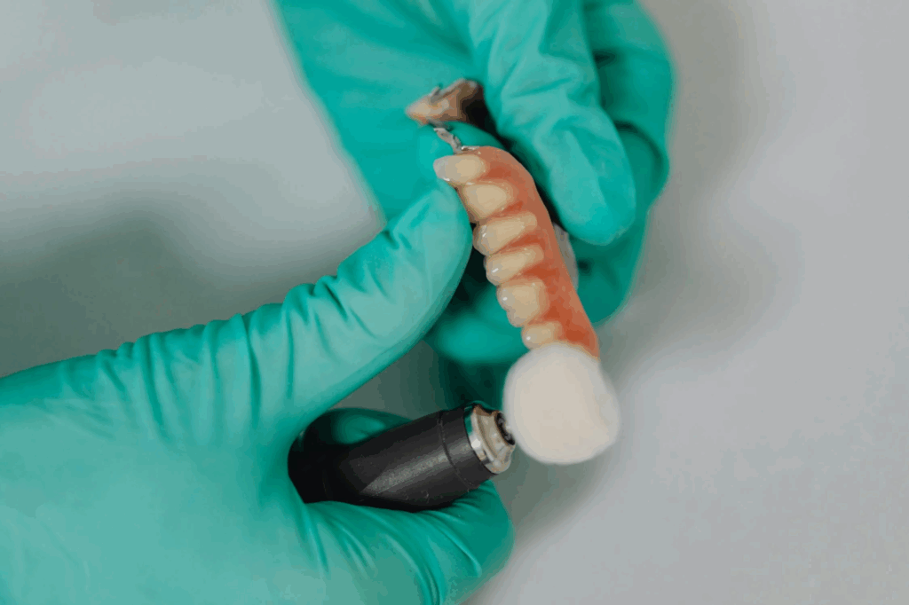 A gloved hand holds a dental implant, with a polishing tool