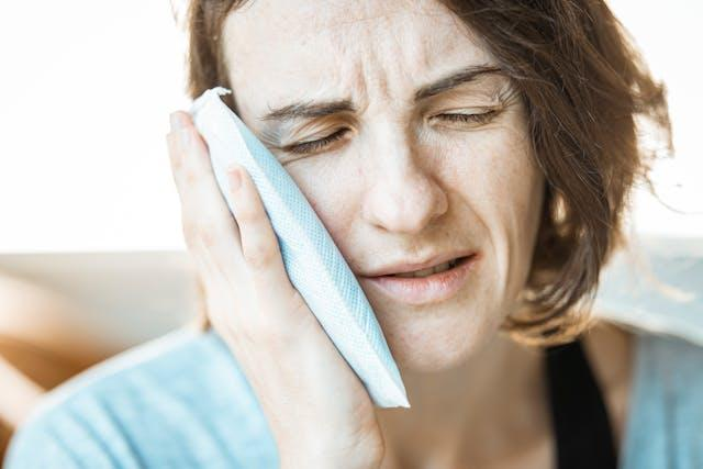 A woman feeling pain at the back of her mouth using an ice pad to treat her tooth pain