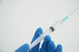 A hand holding a syringe with a needle, wearing blue gloves