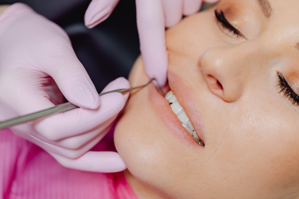 A close-up of a dentist wearing pink gloves examining a woman’s teeth with a dental instrument during a dental checkup