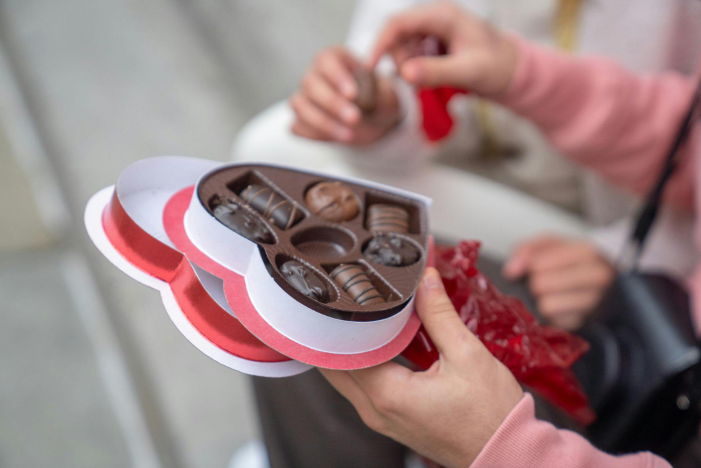 This photo shows a man holding a heart-shaped box of chocolates