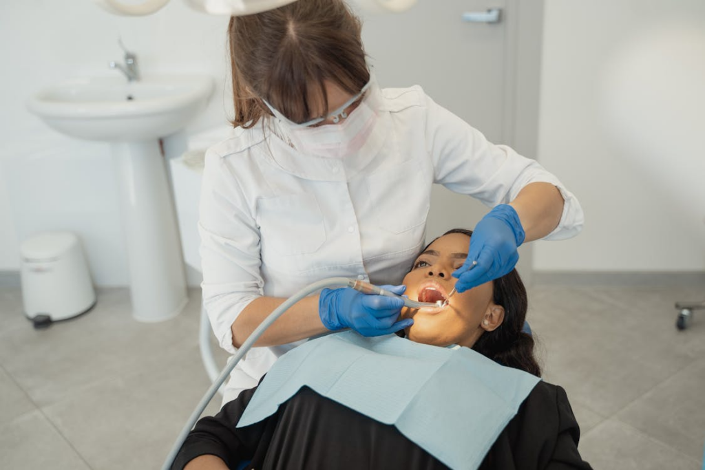 A female dentist wearing a facemask examines a patient's teeth in a dental clinic