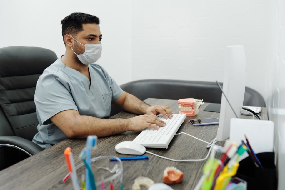 A dentist in a face mask types at a computer in a dental office
